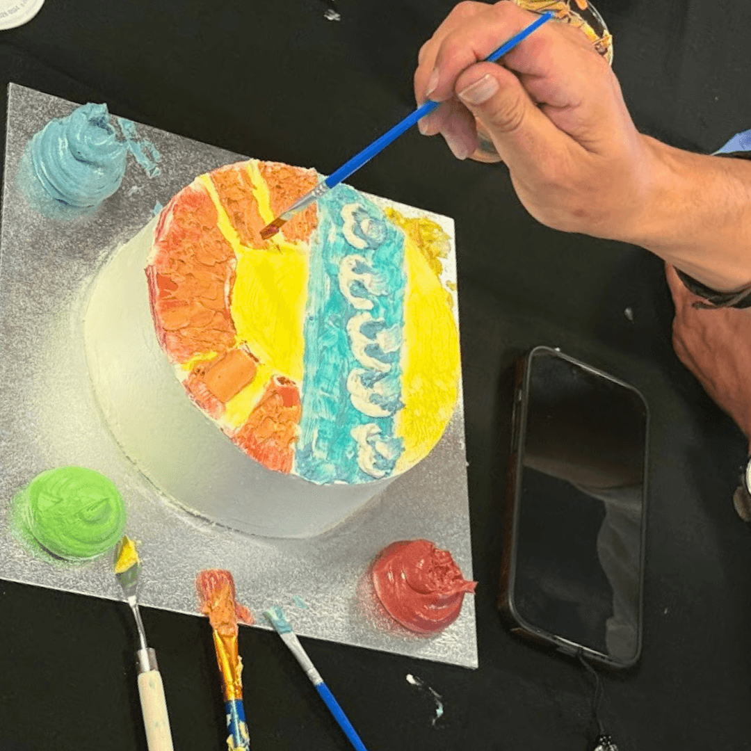Painting a colourful buttercream cake with a fine brush during a workshop
