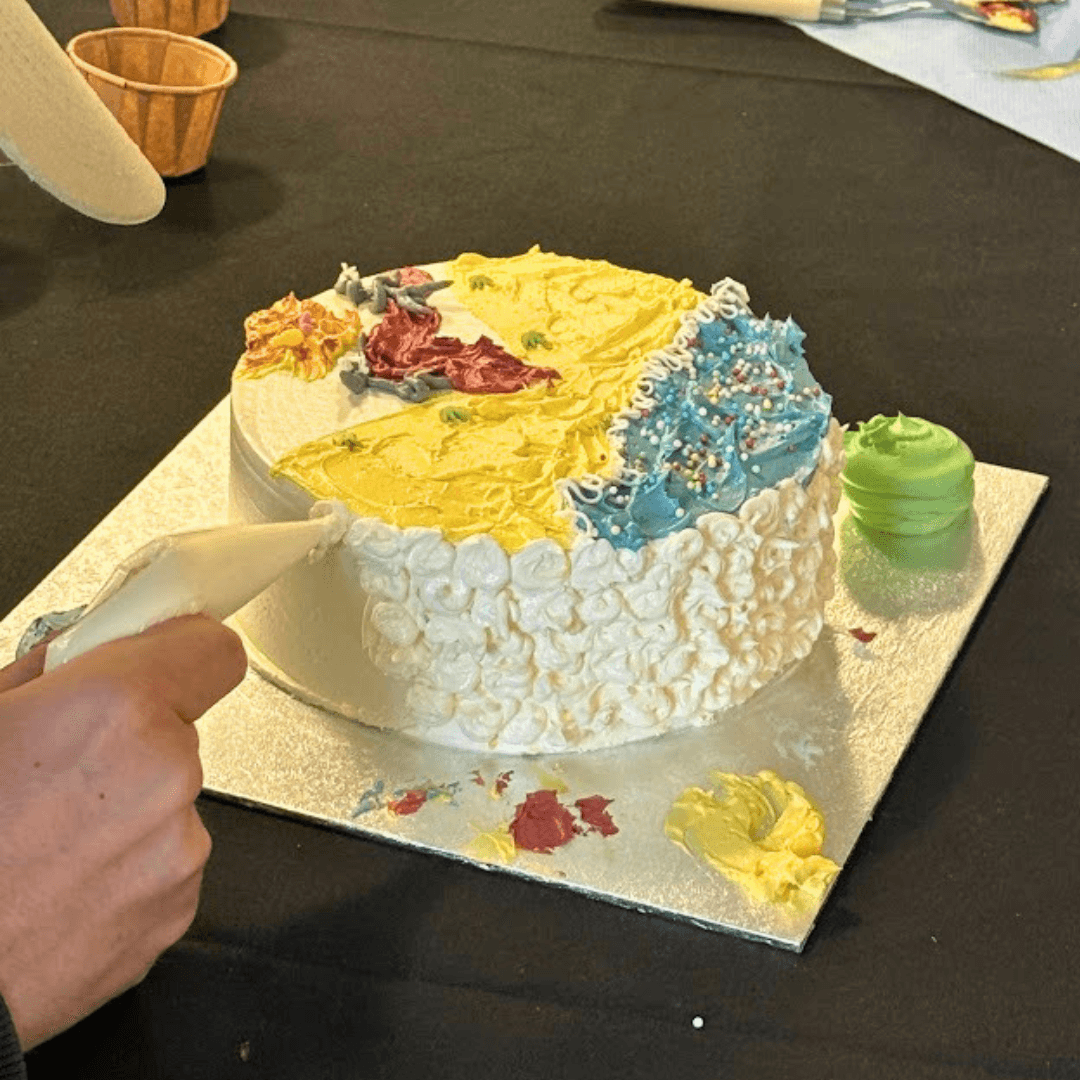Piping white buttercream around the side of a workshop cake