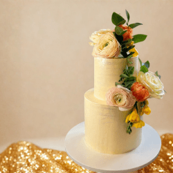 Tall ivory celebration cake decorated with pale flowers and greenery